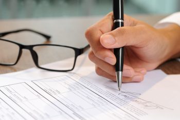 Closeup of woman signing document. Contract and glasses lying on table. Deal concept. Cropped view.